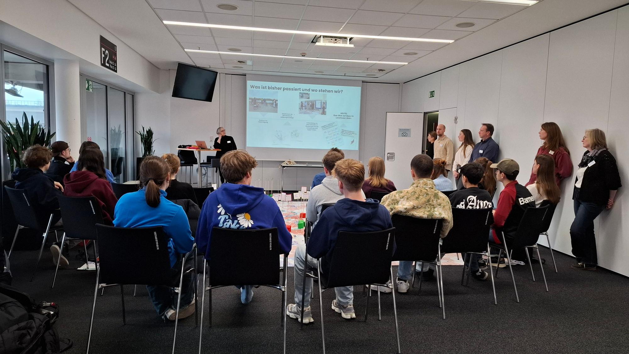 Junge Leute sitzen um einen Tisch vor einem Bildschirm.
