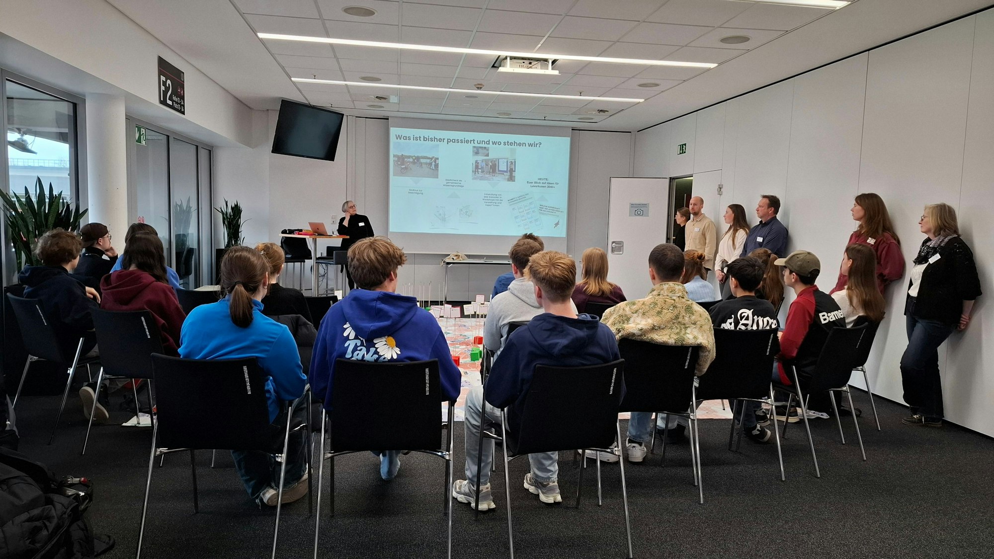 Junge Leute sitzen um einen Tisch vor einem Bildschirm.