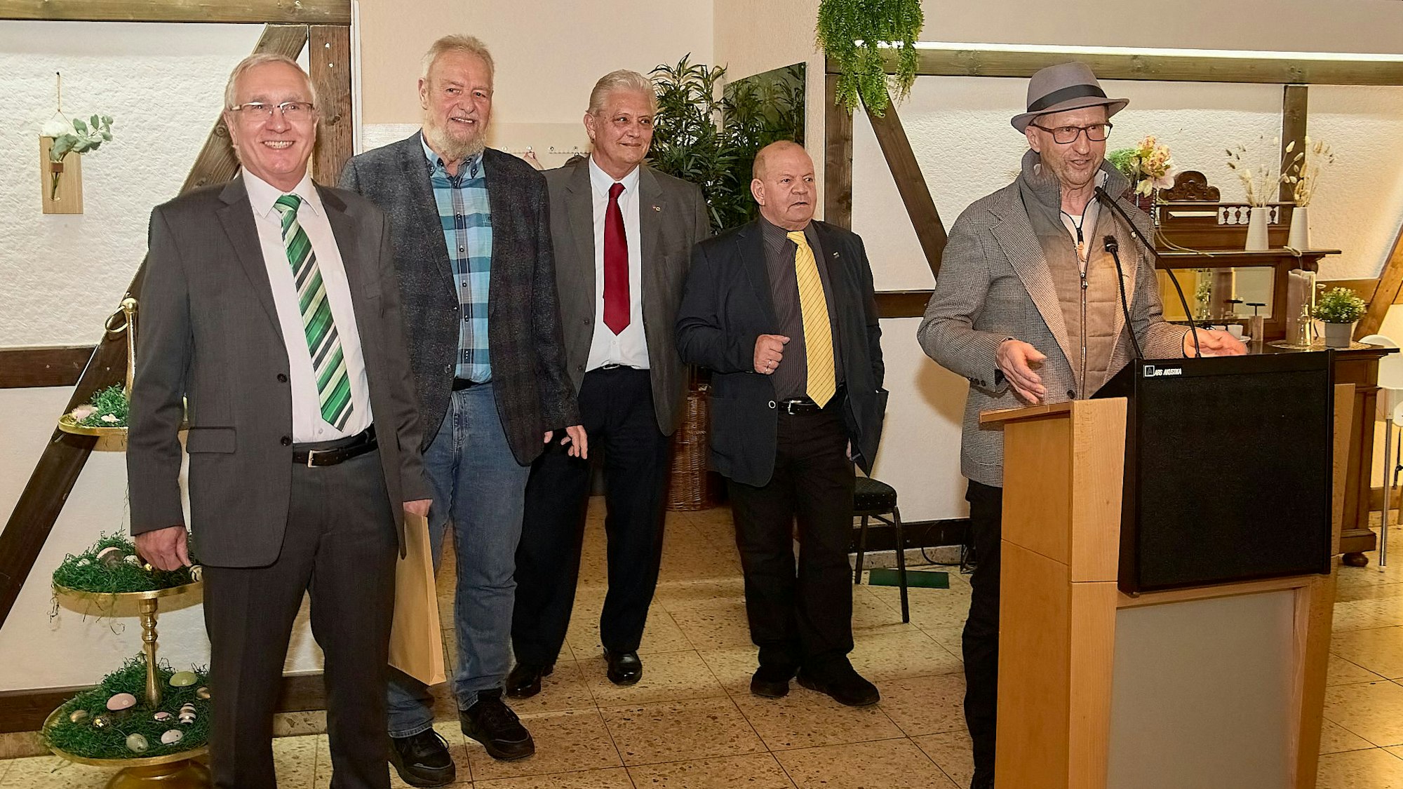 Fünf Männer stehen in den Grenzlandstuben in Hellenthal. Rechts steht Heinz-Bert Weimbs, er spricht in ein Mikrofon.