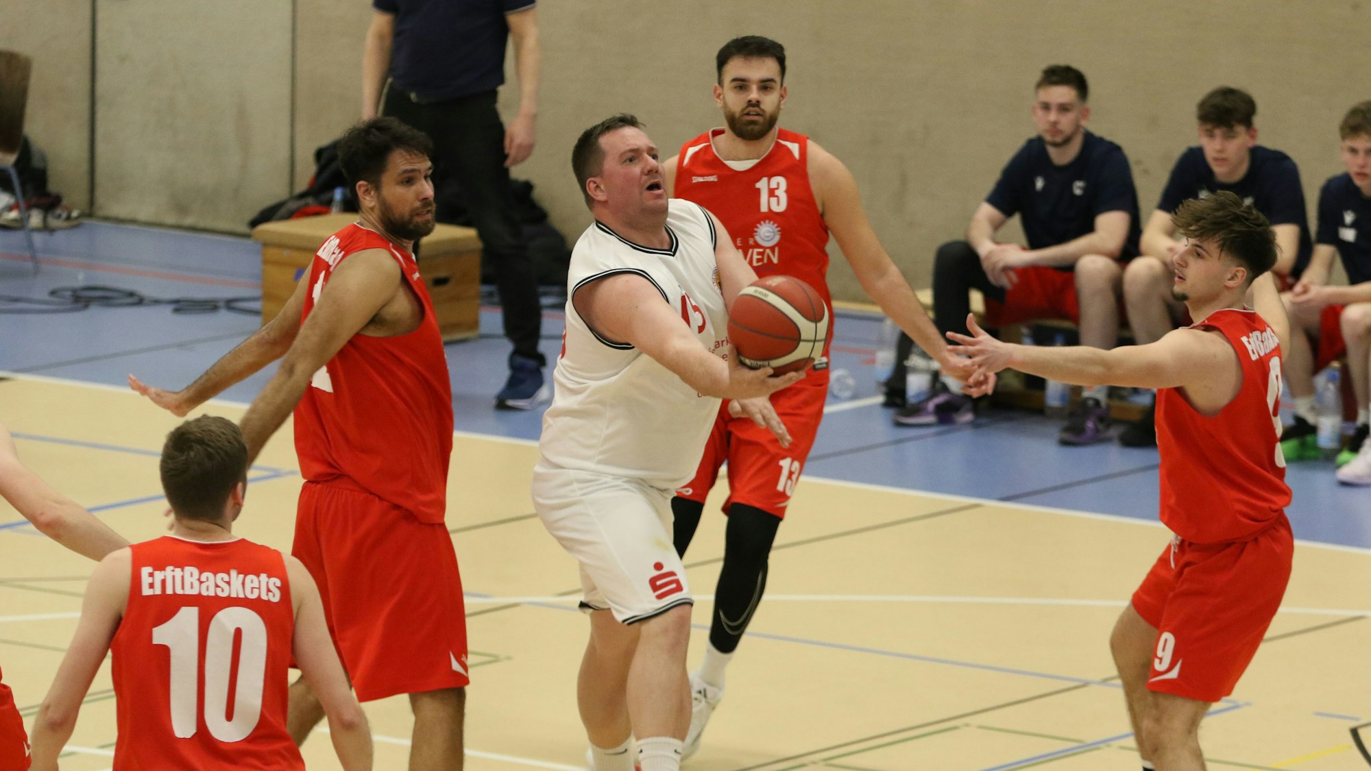 Ein Basketballspieler greift von unten an den Ball. Umringt ist er von vier Gegenspielern.