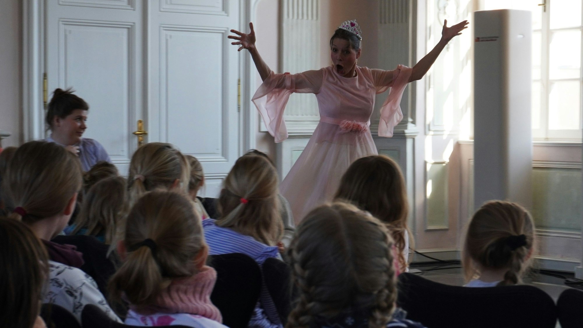 Eine Frau in einem Prinzessinnenkostüm gestikuliert vor einem vornehmlich aus Kindern bestehenden Publikum.