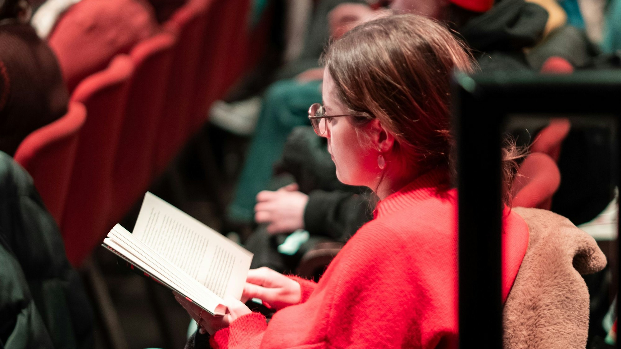 Eine Zuschauerin sitzt im Publikum und liest ein Buch.
