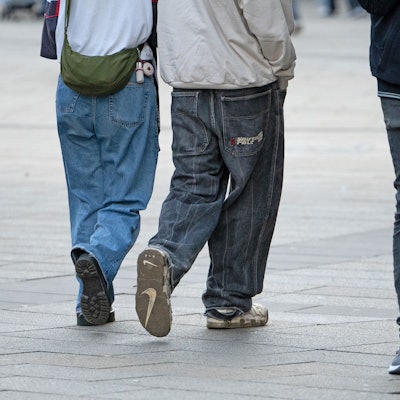 Drei Jugendliche in Jeans gehen durch die Innenstadt. Einer hält eine Zigarette in der Hand.