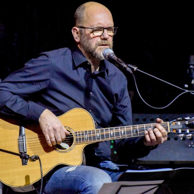 Ein Mann sitzt mit einer Gitarre auf einer Bühne.