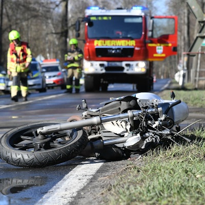 Ein Motorrad liegt am Straßenrand und im Hintergrund sichern die Feuerwehr und die Polizei die Unfallstelle.