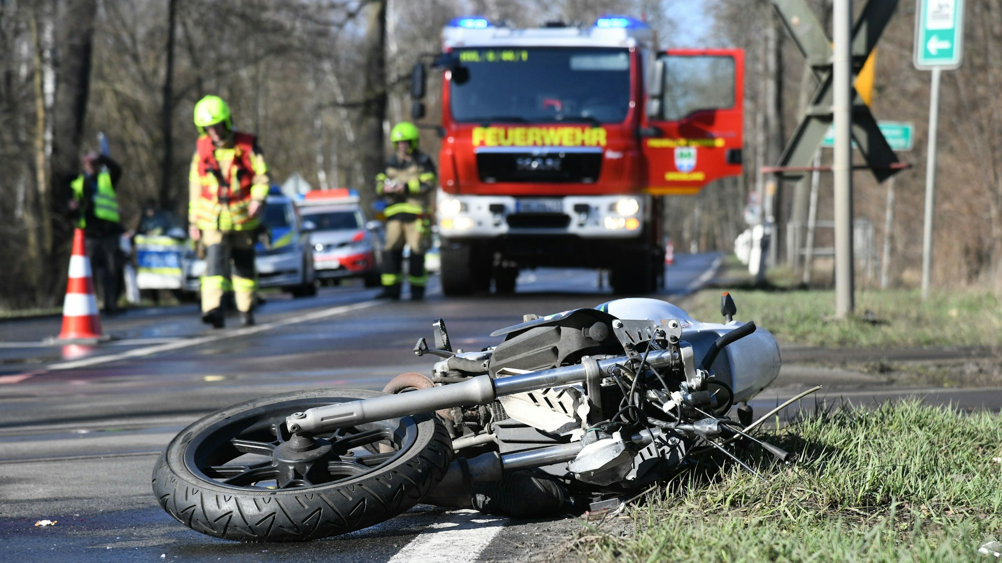 Ein Motorrad liegt am Straßenrand und im Hintergrund sichern die Feuerwehr und die Polizei die Unfallstelle.