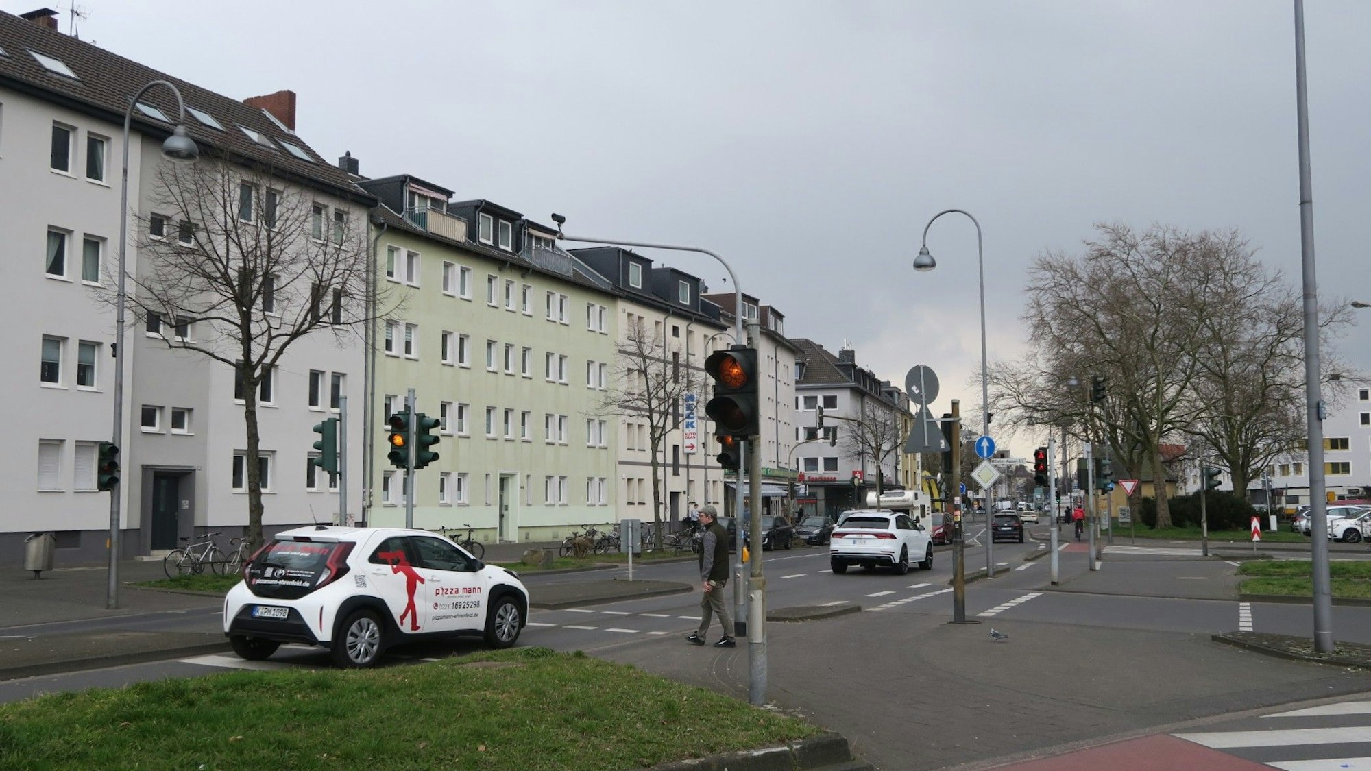 Autos fahren über eine Straße, ein Fußgänger will an einer Ampel die Straße überqueren.