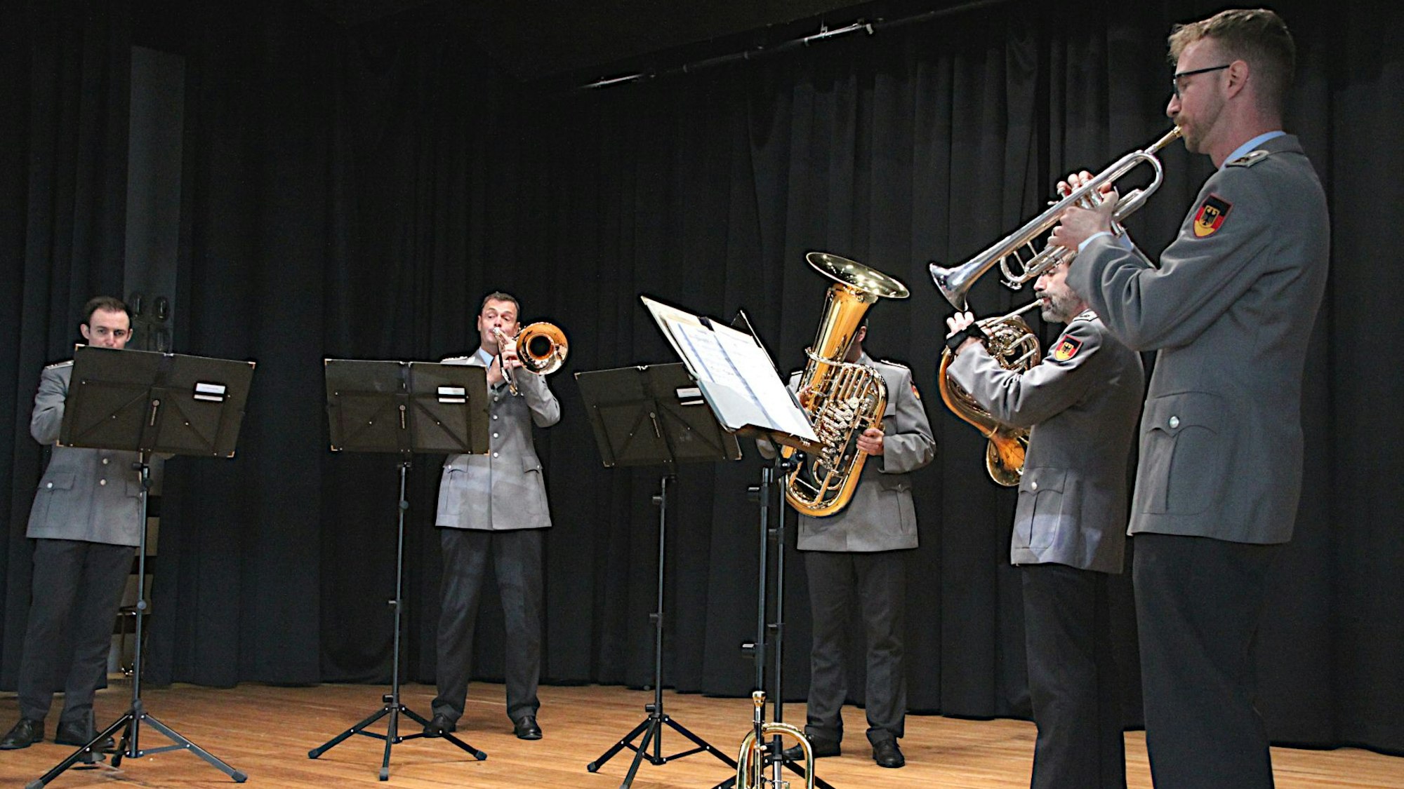 Die fünf Musiker stehen mit ihren Instrumenten hinter Notenständern und musizieren. Alle tragen Uniform.