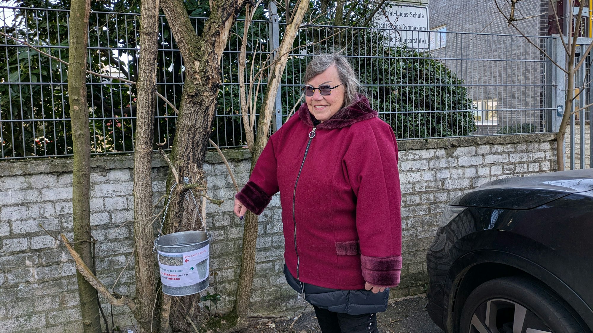 Eine Frau steht neben einem improvisierten Ascheimer, den sie an den Zweig eines Strauchs gehängt hat.