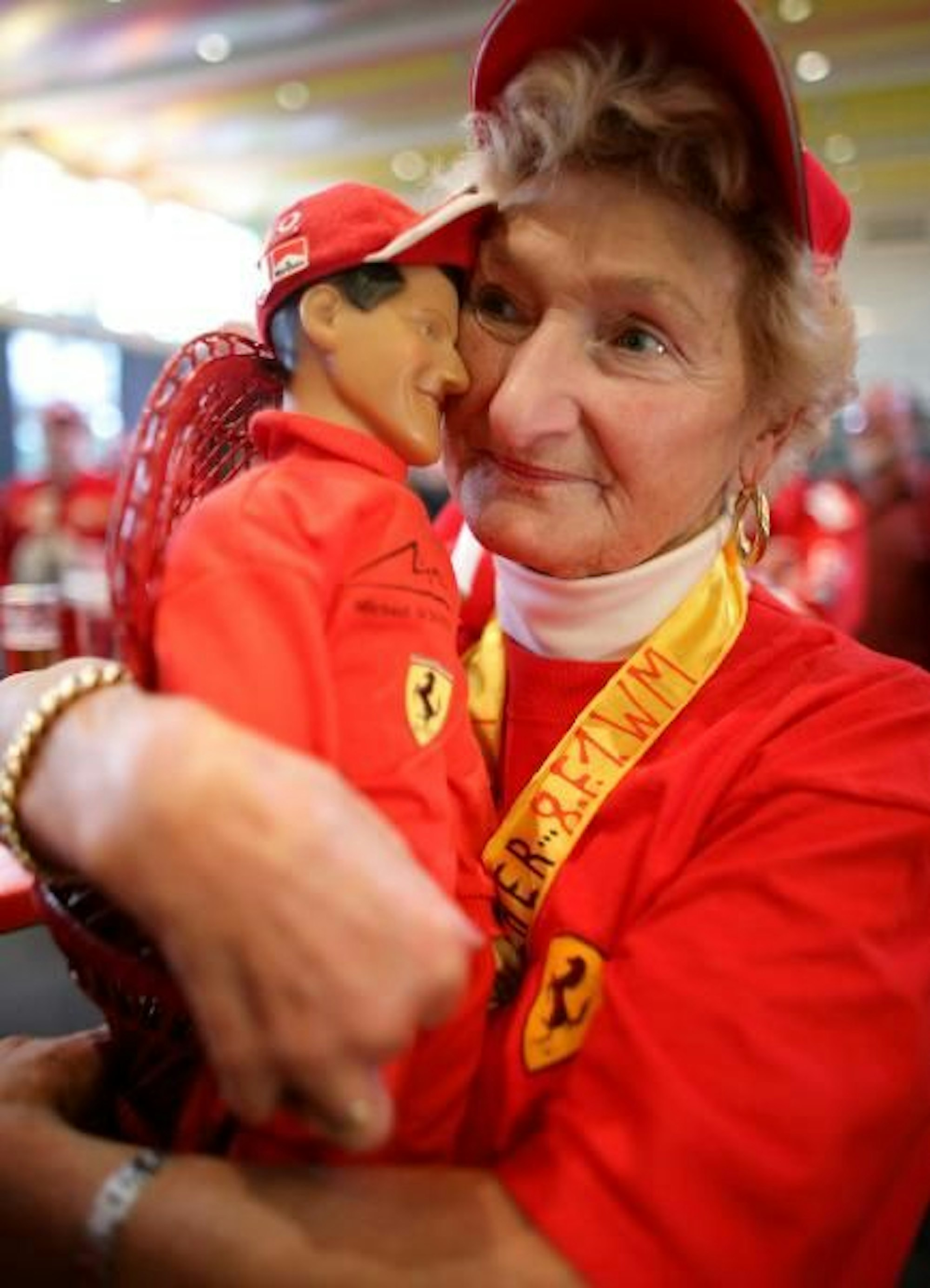 Erika Klütsch hält in der Jahnhalle in Kerpen vor einer Großbildleinwand eine Puppe von Weltmeister Michael Schumacher im Arm.
