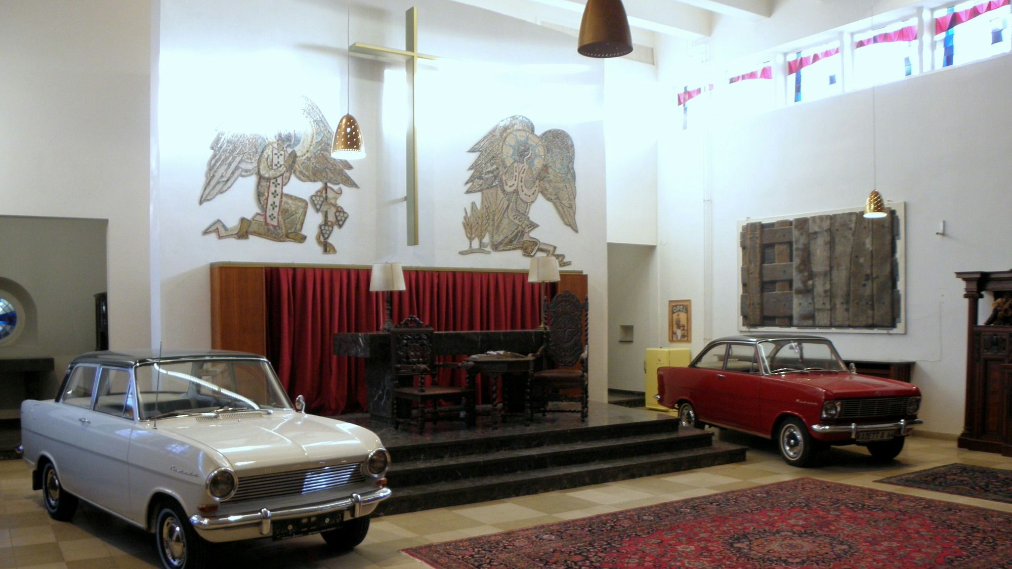Zwei Wagen stehen links und rechts neben dem alten Altar, darüber ist ein Kreuz an der Wand angebracht.