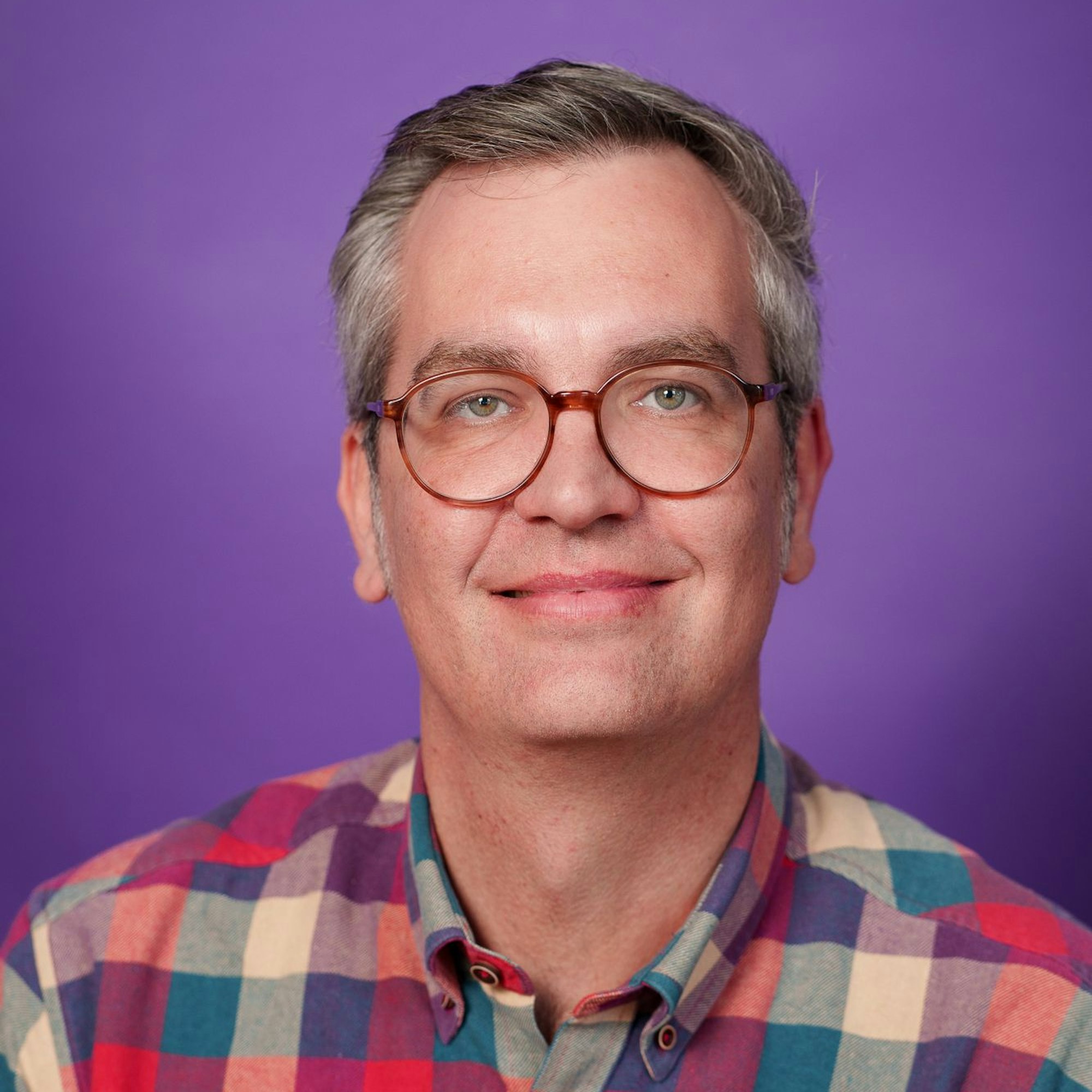 Lars Wolfram in Karohemd mit Brille vor lila Hintergrund