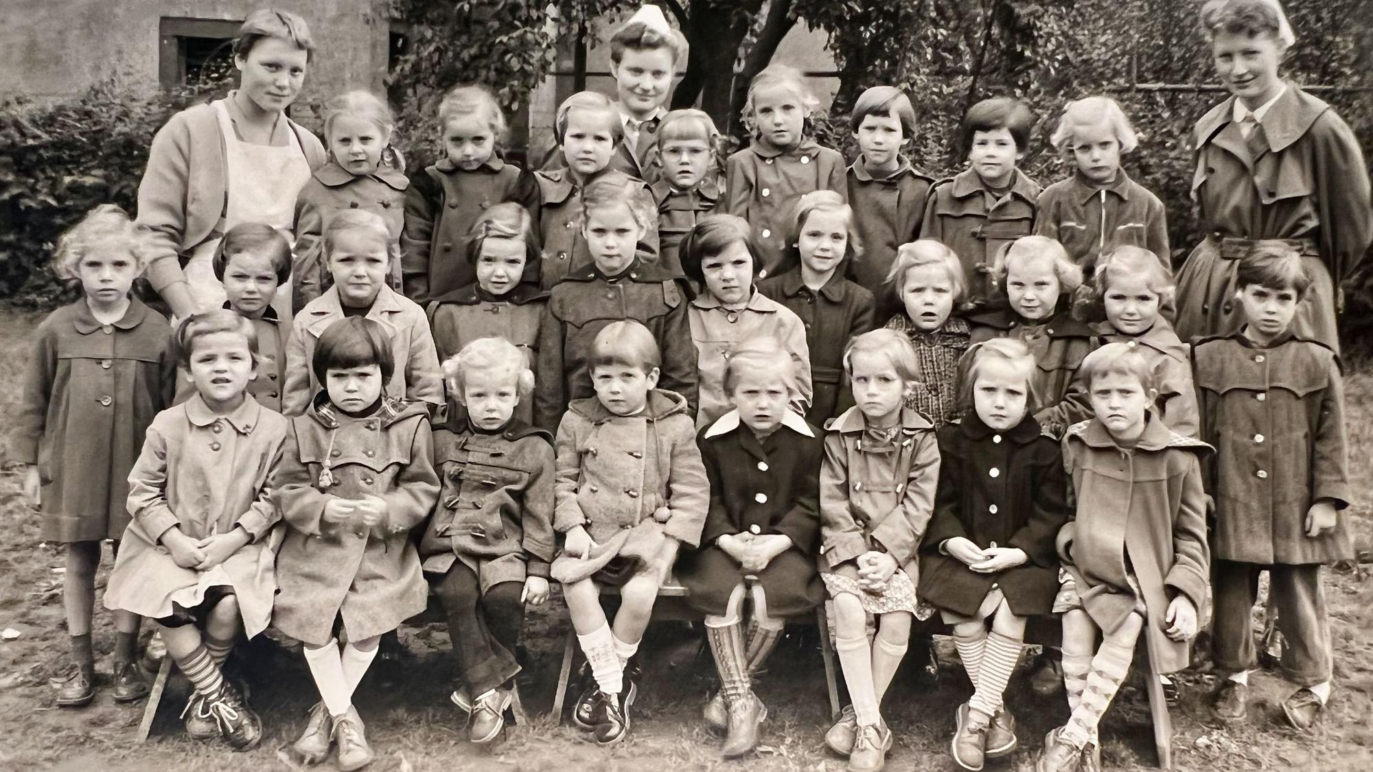 Auf dem SW-Bild ist eine Gruppe von Kindern mit Pflegerinnen zu sehen.