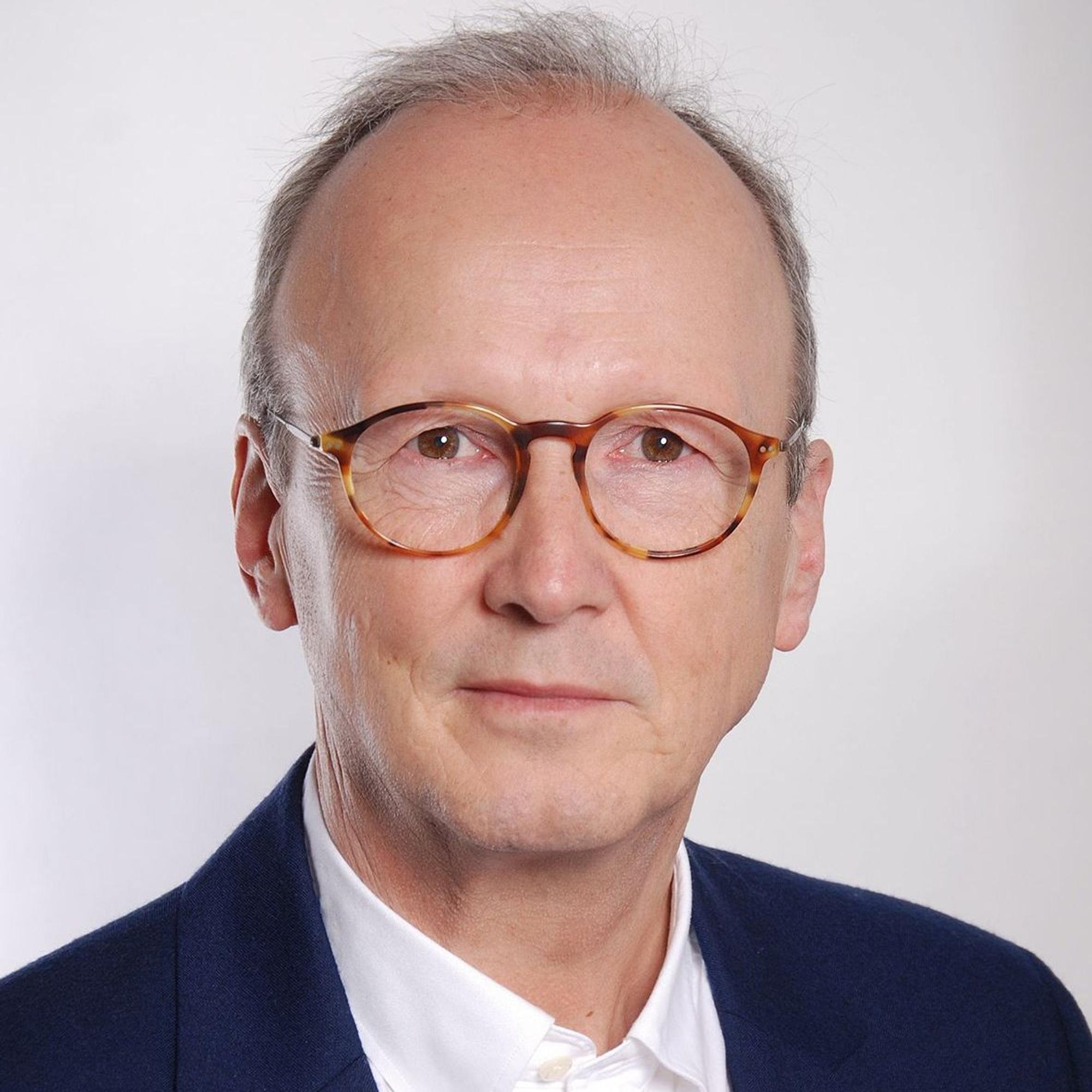 Auf dem Bild ist das Portrait eines Mannes in einem blauen Sakko zu sehen.