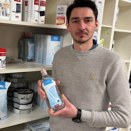 Auf dem Bild ist ein Mann mit einer Flasche Pflegemittel in der Hand zu sehen.