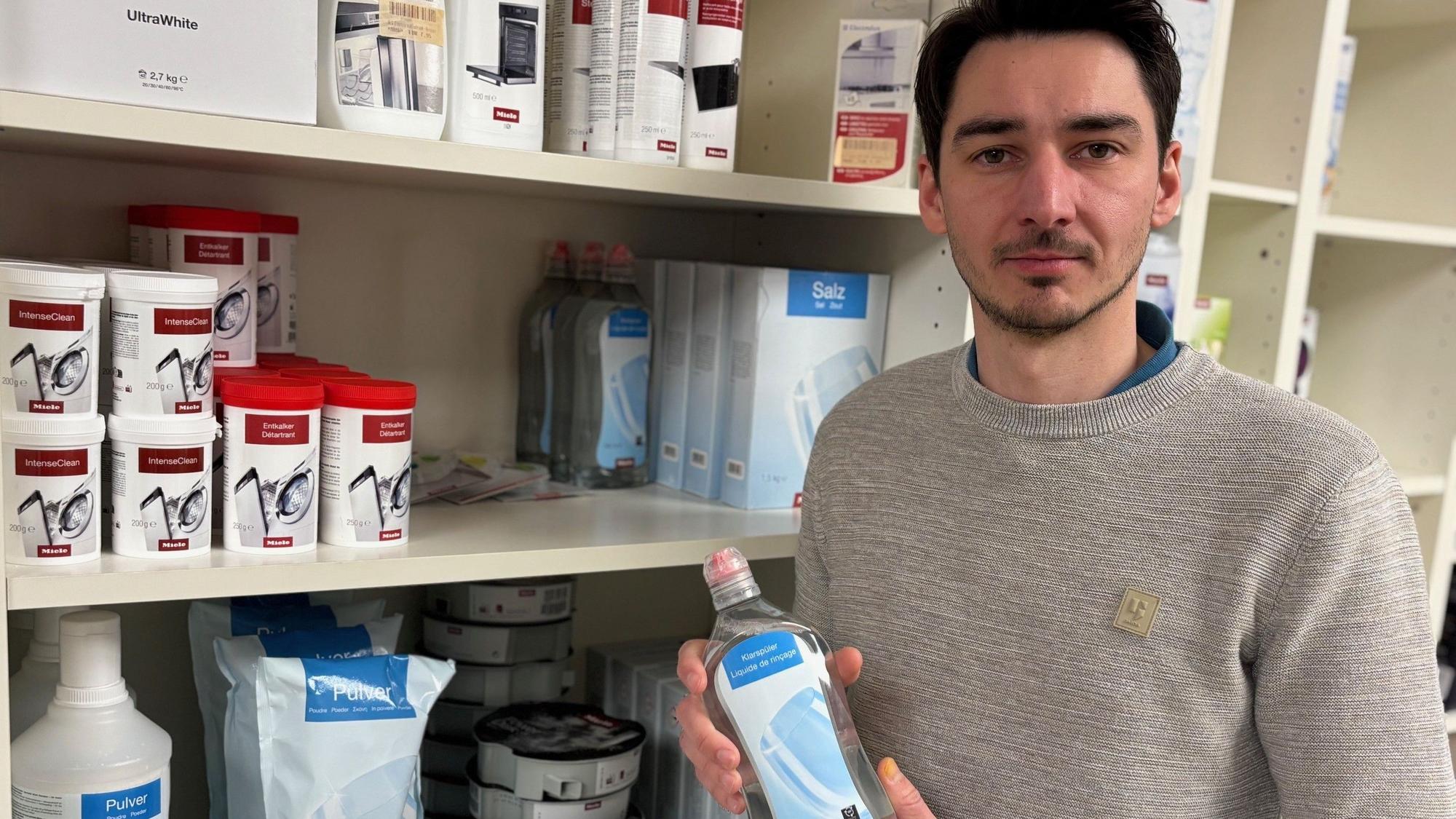 Auf dem Bild ist ein Mann mit einer Flasche Pflegemittel in der Hand zu sehen.
