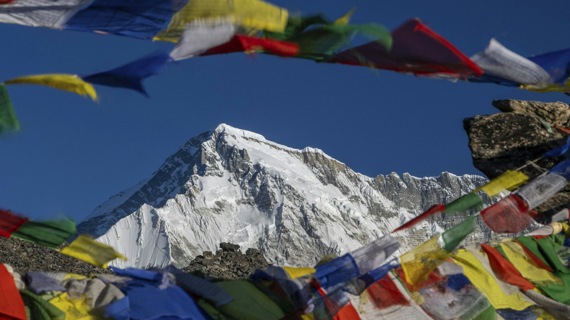 Der Achttausender Cho Oyu kurz nach Sonnenaufgang mit einigen bunten buddhistischen Gebetsfahnen im Vordergrund, die den Gipfel des Gokyo Ri, eines beliebten Trekkinggipfels in der Everest-Region, markieren.