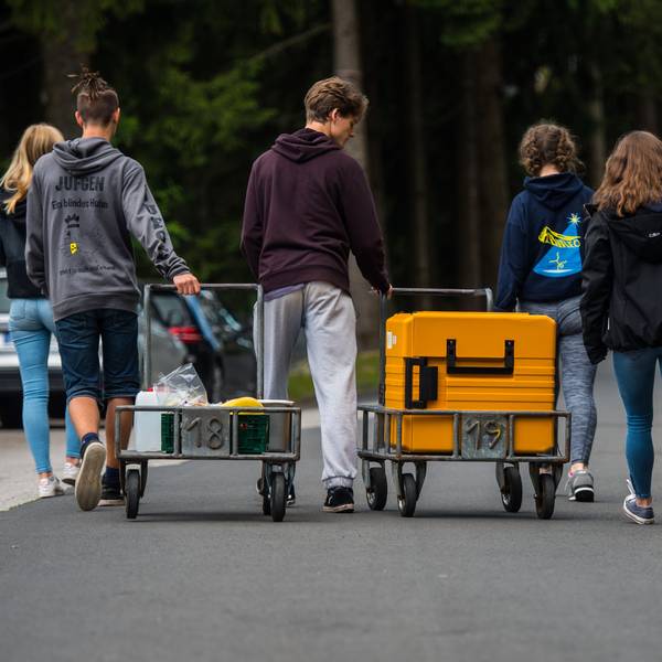 Eine Schülergruppe bringt während einer Klassenfahrt einen Transportwagen mit Essen in ihre Unterkunft.