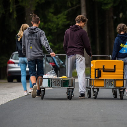 Eine Schülergruppe bringt während einer Klassenfahrt einen Transportwagen mit Essen in ihre Unterkunft.