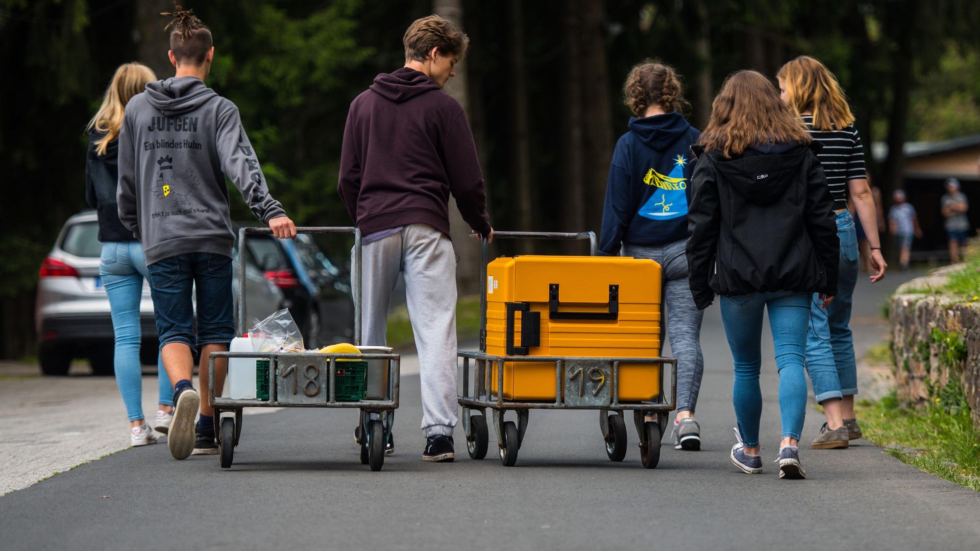 Eine Schülergruppe bringt während einer Klassenfahrt einen Transportwagen mit Essen in ihre Unterkunft.