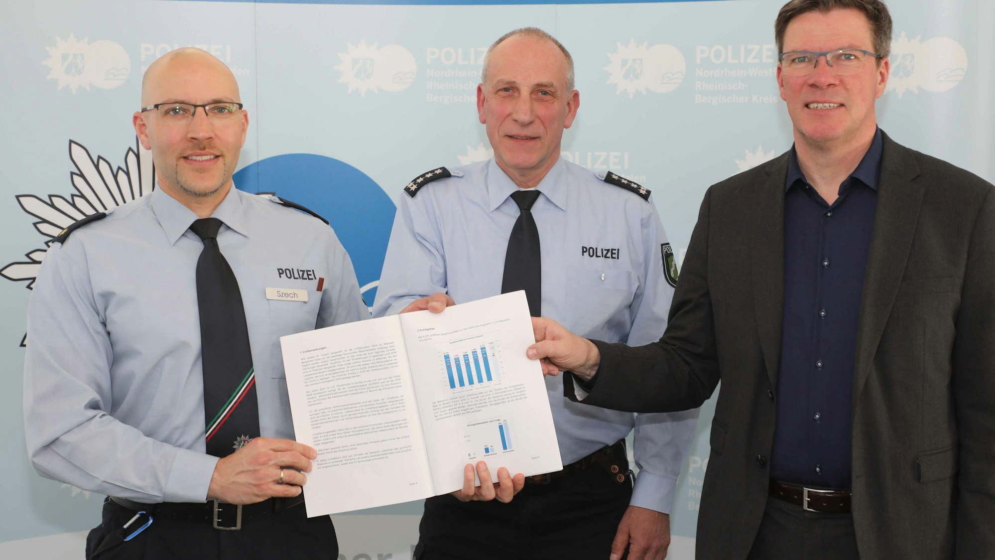 Markus Szech (Leiter Direktion Verkehr), Thomas Schliwitzki (Leiter Verkehrsdienst und Prävention & Opferschutz) und Landrat Stephan Santelmann halten die Verkehrsunfallbilanz für Rhein-Berg 2024.