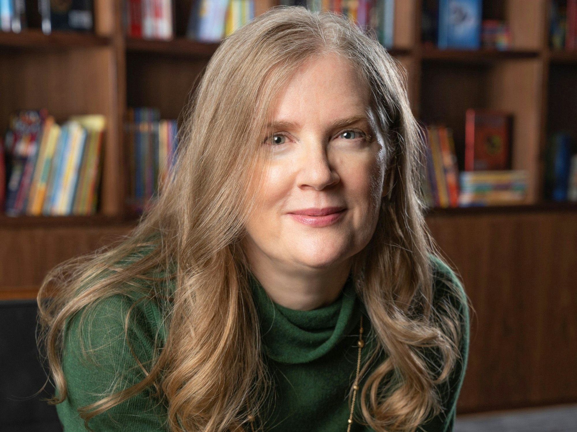 Die amerikanische Bestseller-Autorin Suzanne Collins schaut vor einem Bücherregal in die Kamera.