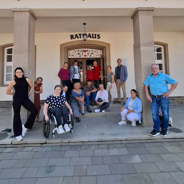 Eine Gruppe von Menschen, darunter eine Frau im Rollstuhl, steht vor dem Rathaus.