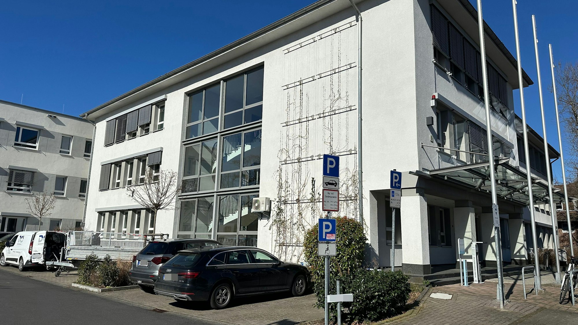 Ein Verwaltungsgebäude aus den 60er Jahren, davor einige Stellplätze für Autos.