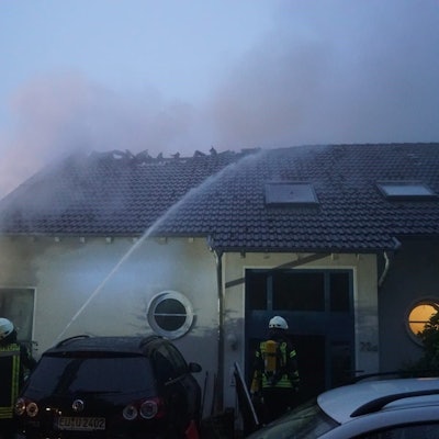 Feuerwehrleute bekämpfen den Brand des Hauses, dessen Dach bereits zum Teil zerstört worden ist.