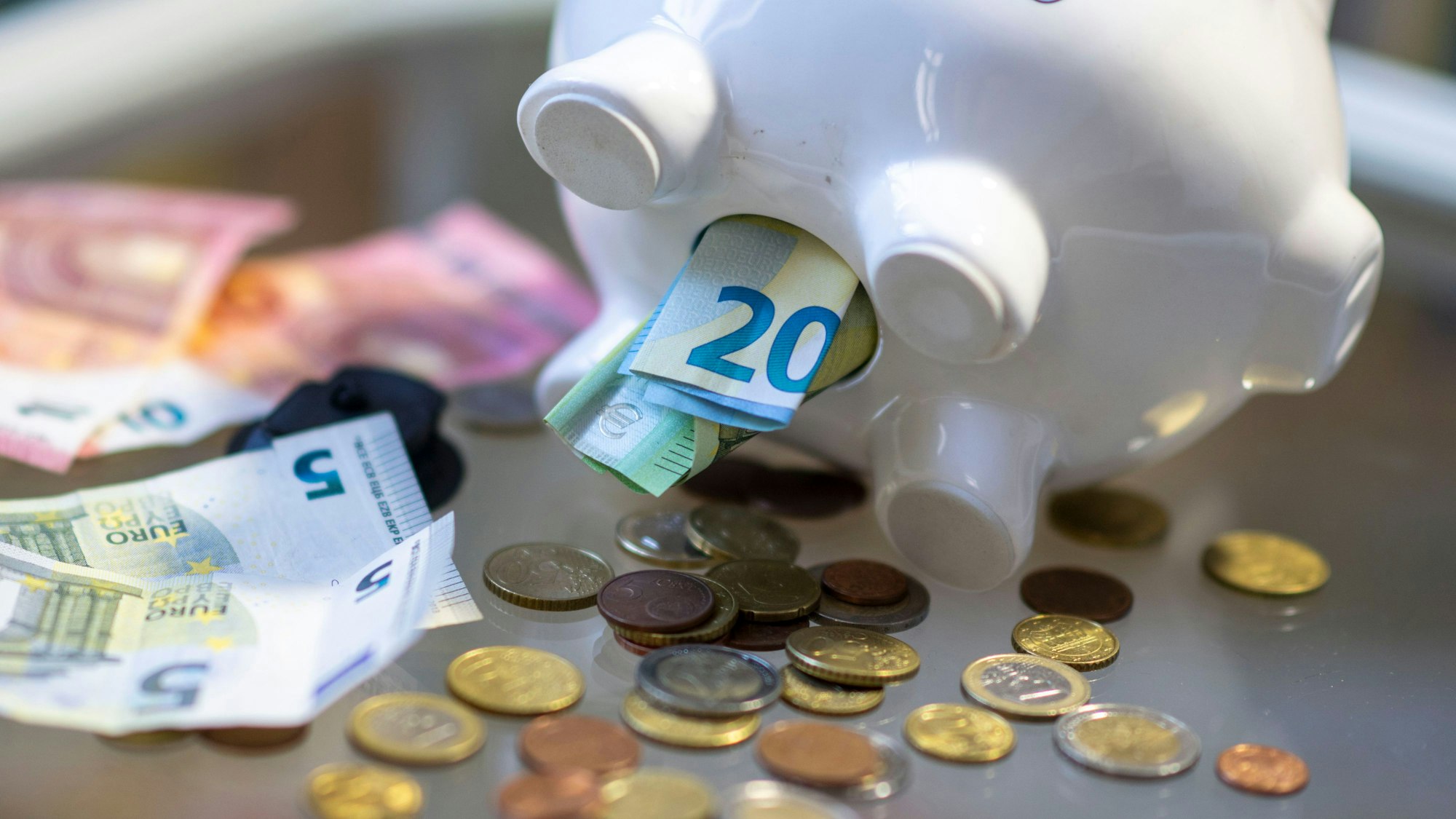 Aus einem umgekippten Sparschwein fallen Scheine und Münzgeld heraus.