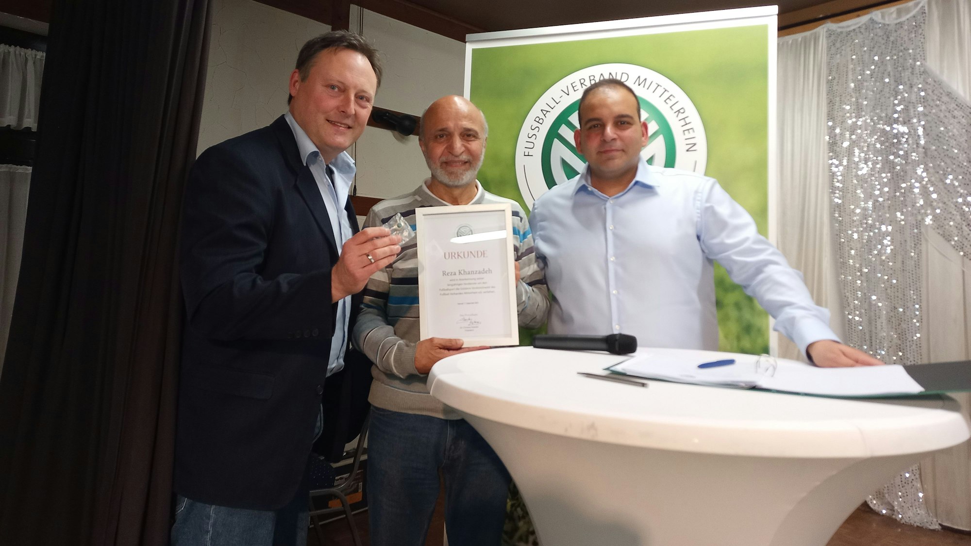 Schiedsrichter Reza Khanzadeh (M.) erhält für seine Verdienste um den Fußball die Goldene Verdienstnadel des FVM aus den Händen von Michael Bernhardt (l.), , und Cem Sayilgan..