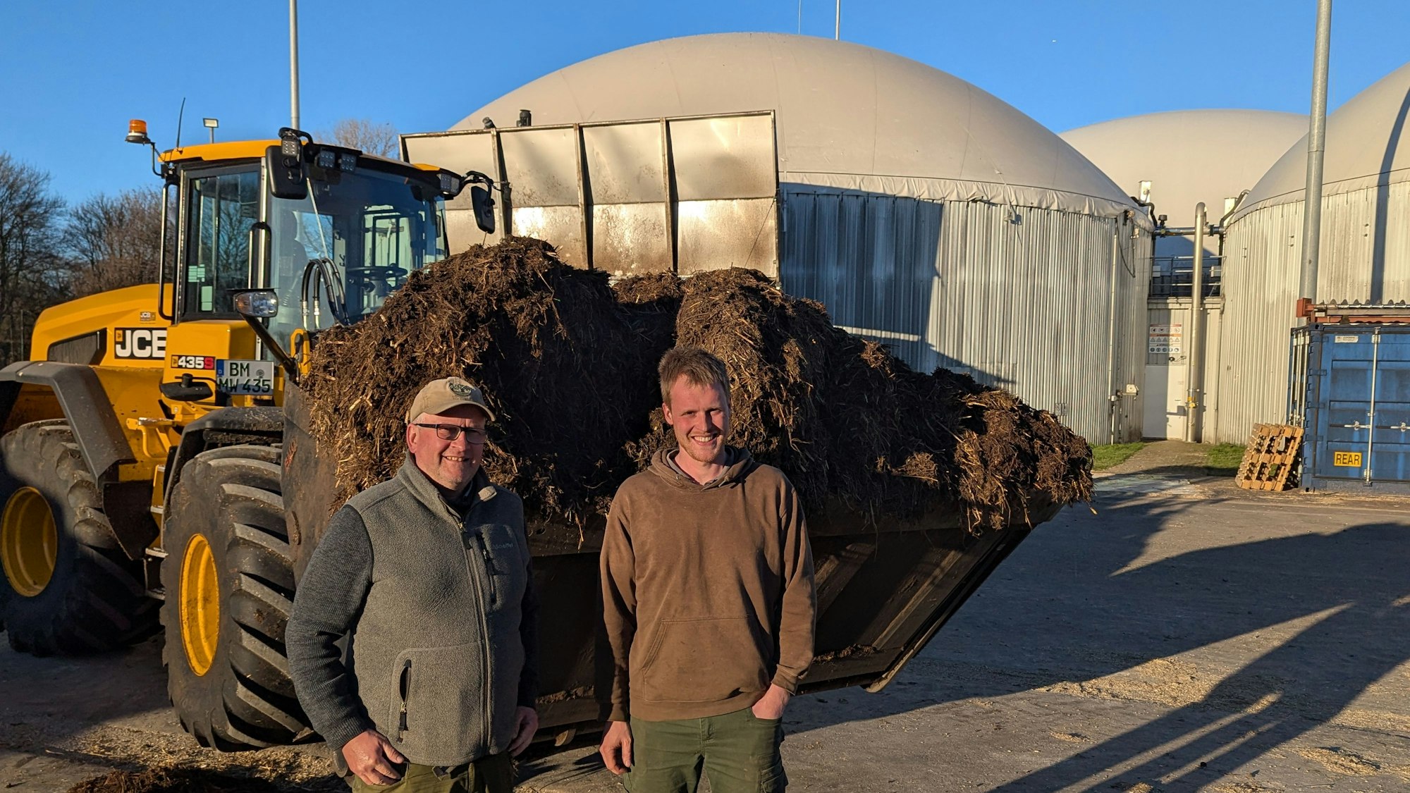 Das Foto zeigt den Landwirt und den Maschinenbauingenieur vor der Biogasanlage.
