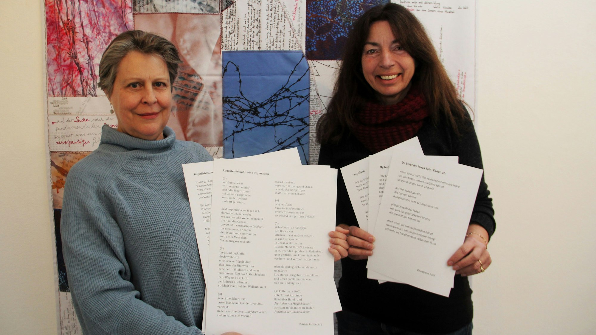 Zwei Frauen halten weiße Blätter mit Lyrik in den Händen. Im Hintergrund ist eine Patchwork-Decke zu sehen.