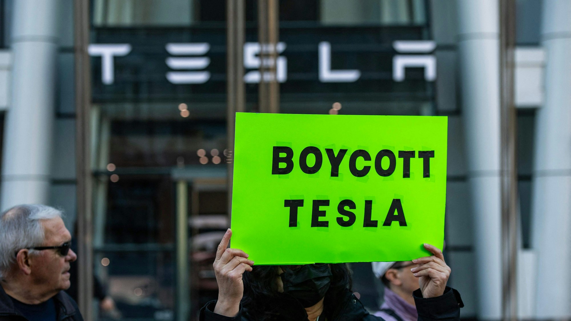Auf dem Schild sind Protestierende zu sehen, die ein Schild mit einem Boykott- des Autoherstellers Tesla vor einer Tesla-Filiale des US-Autobauers in die Höhe halten. Foto: Joseph Prezisio/AFP