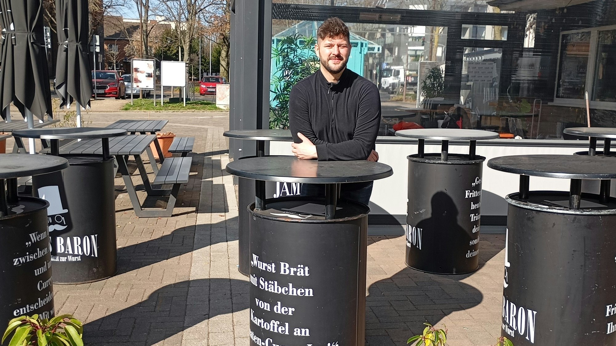 Ein Mann lehnt sich auf einen Stehtisch, er steht im Freien.