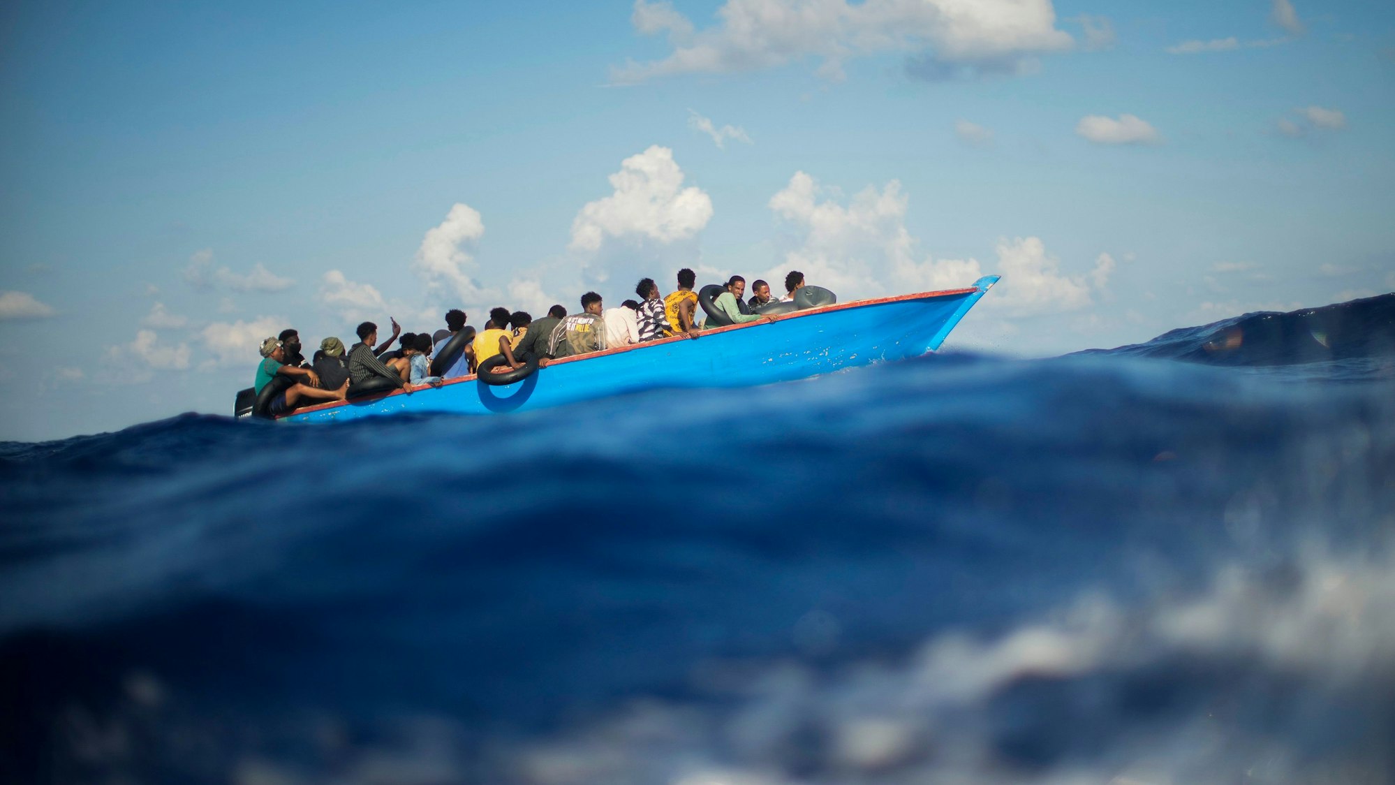 Migranten sitzen in einem Holzboot im Mittelmeer.