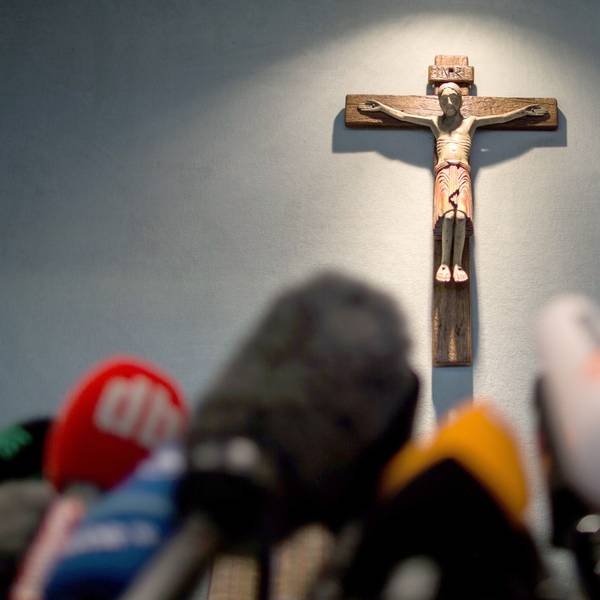 Ein Kreuz hängt einen Tag nach dem Absturz bei einer Pressekonferenz im Rathaus in Haltern am See über Mikrofonen.