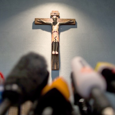 Ein Kreuz hängt einen Tag nach dem Absturz bei einer Pressekonferenz im Rathaus in Haltern am See über Mikrofonen.