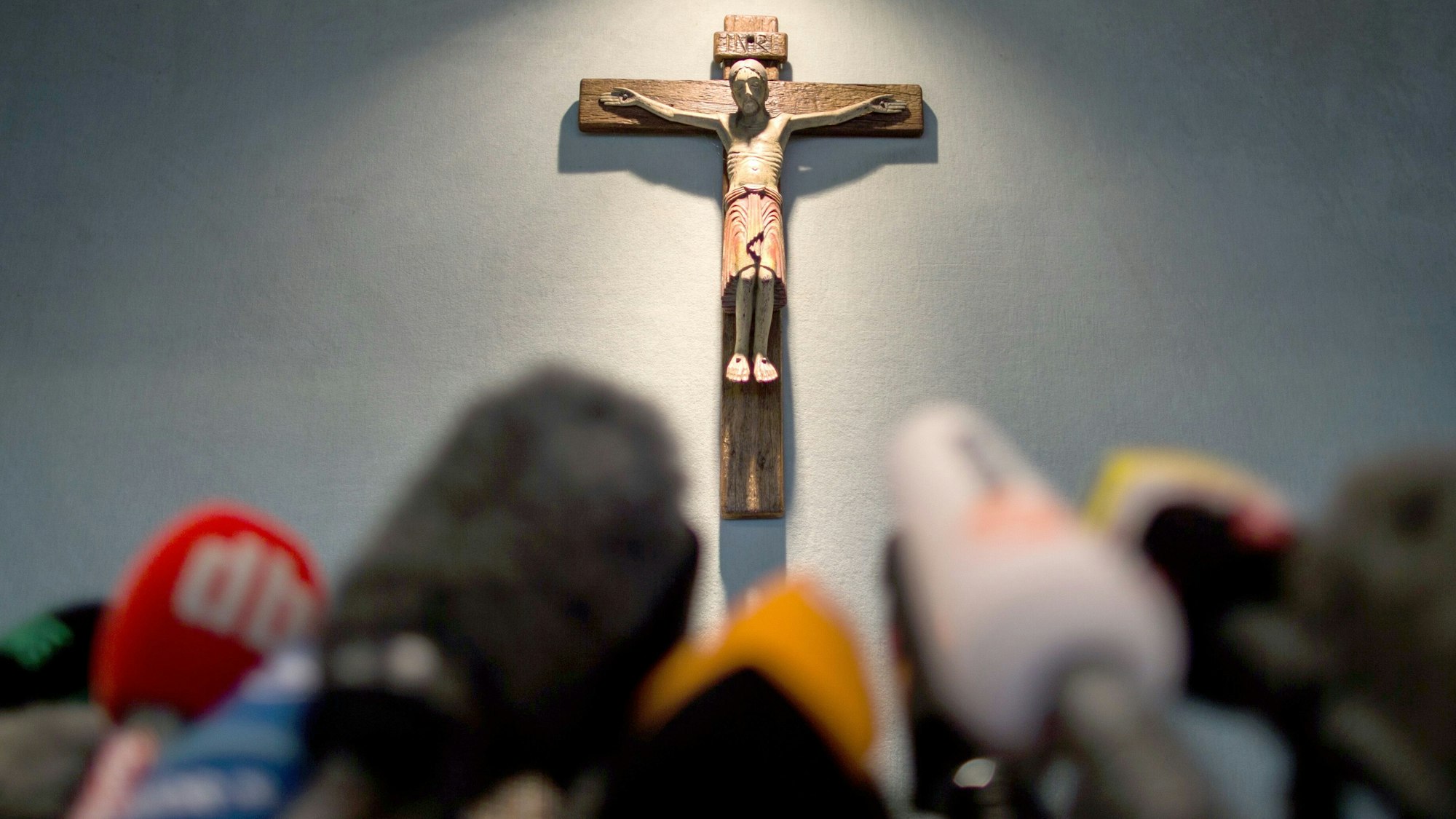 Ein Kreuz hängt einen Tag nach dem Absturz bei einer Pressekonferenz im Rathaus in Haltern am See über Mikrofonen.