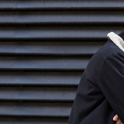 Ein Jugendlicher vor einer schwarzen Wand in schwarzem Pullover schaut traurig nach unten.