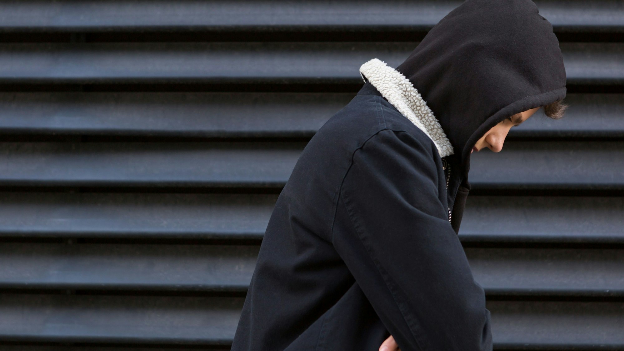 Ein Jugendlicher vor einer schwarzen Wand in schwarzem Pullover schaut traurig nach unten.