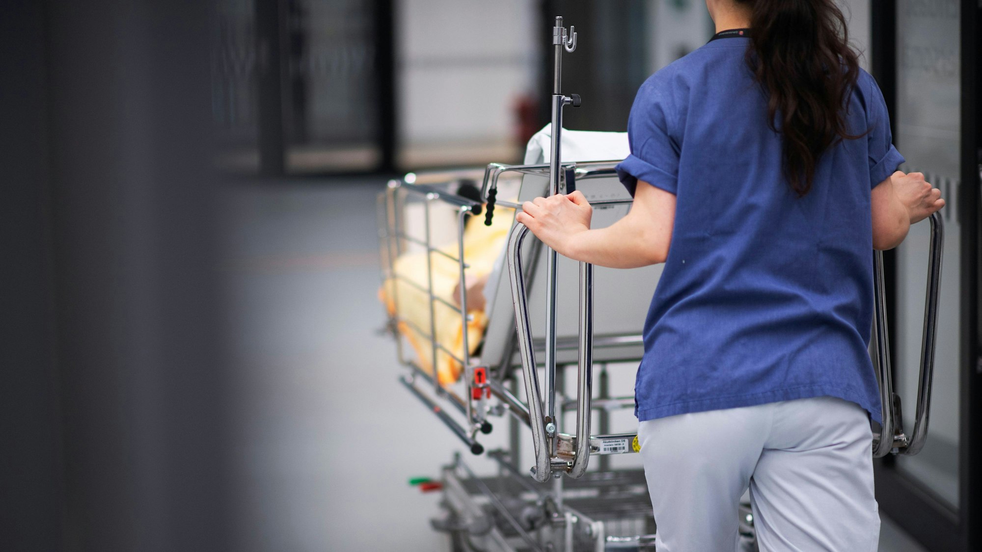 Eine Krankenpflegerin schiebt einen Patienten in einen Krankenhausflur.