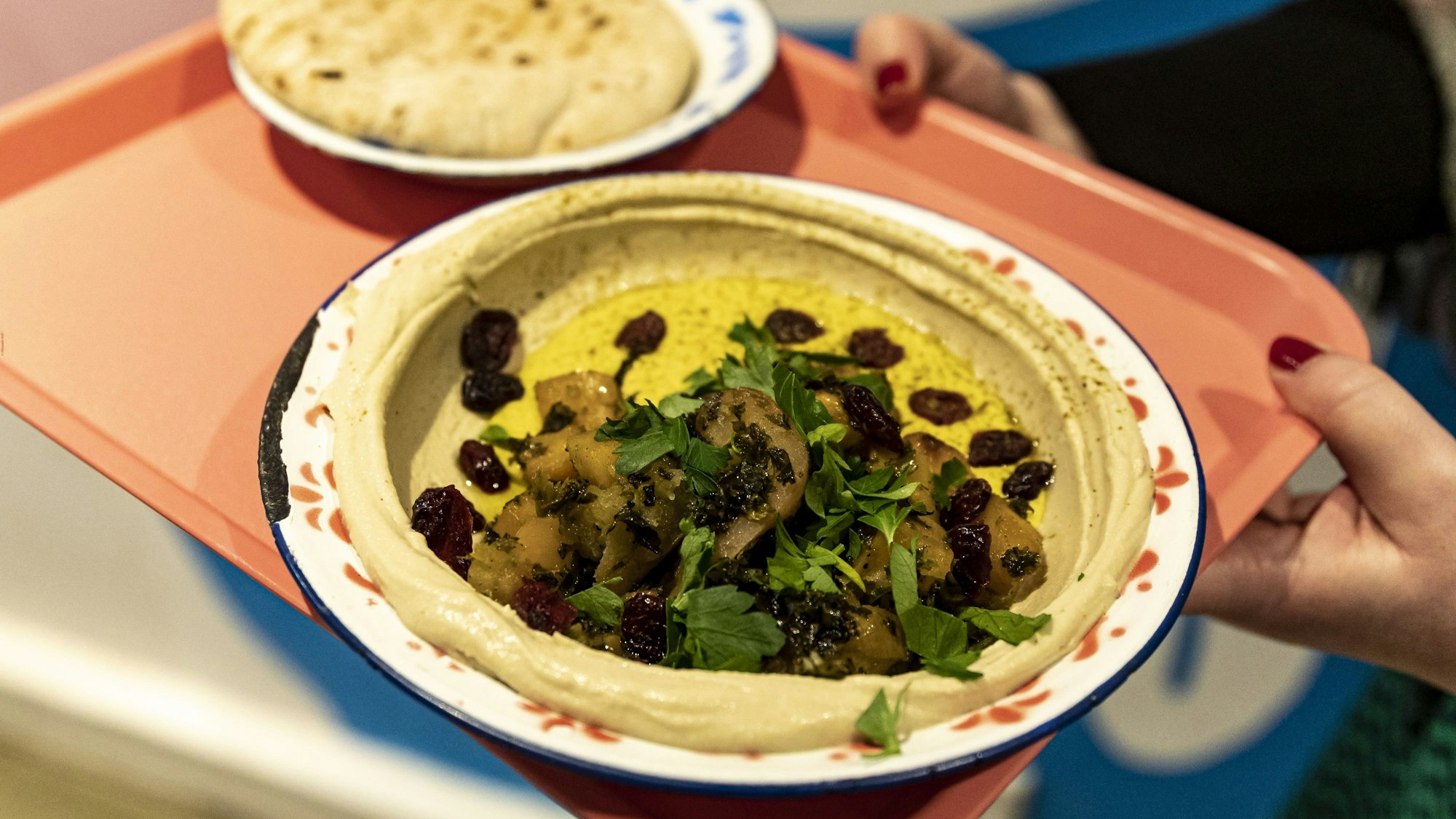 Hummus mit Toppings auf einem Teller, daneben Pitabrot