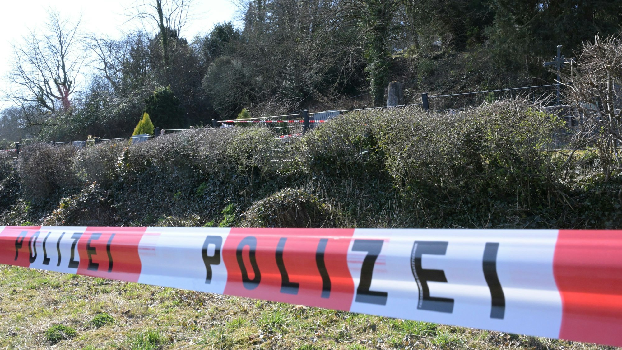 Ein rot-weiße Flatterband mit der Aufschrift Polizei hängt vor dem Friedhofsgelände in Rösrath-Hoffnungsthal.
