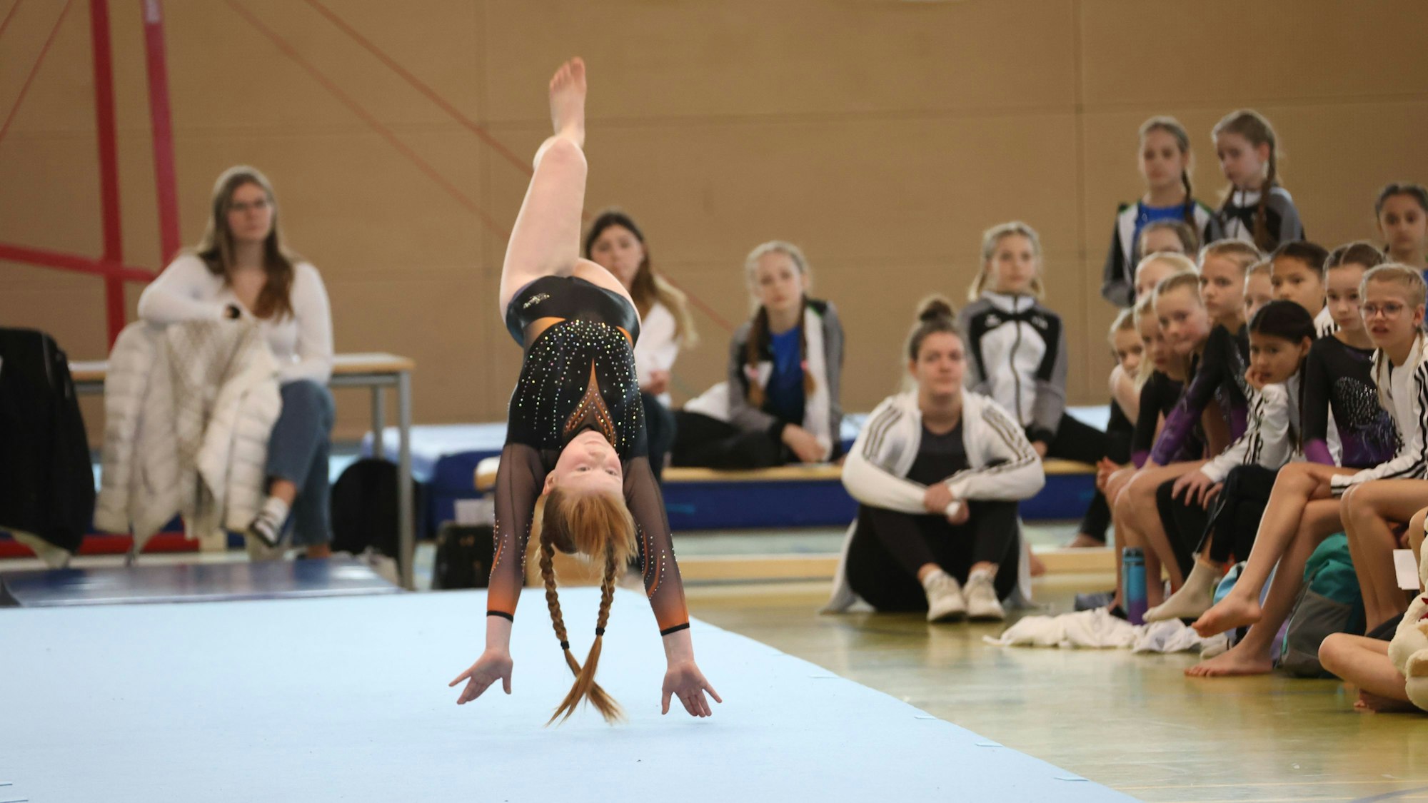 Eine Turnerin macht einen Handstandüberschlag. Die Zuschauer sind gebannt.