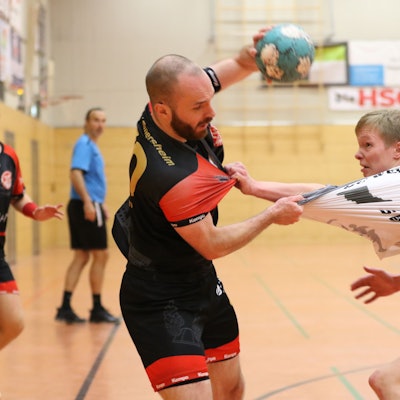 Simon Schöller hält mit der linken Hand den Ball in die Höhe und greift mit der rechten nach dem Trikot seines Gegenspielers, der ihn am Schlafittchen gepackt hat.