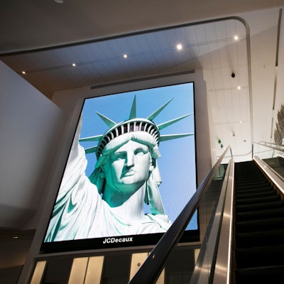 Ein elektronisches Bildschirmbild der Freiheitsstatue begrüßt ankommende Reisende auf einer Rolltreppe im Terminal B des Flughafens LaGuardia.