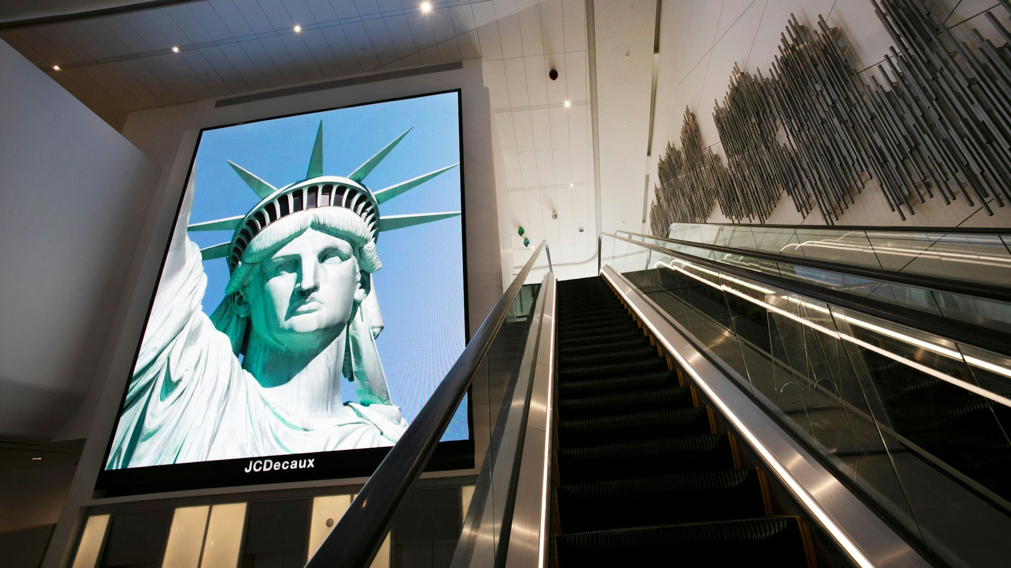 Ein elektronisches Bildschirmbild der Freiheitsstatue begrüßt ankommende Reisende auf einer Rolltreppe im neuen Terminal B des Flughafens LaGuardia. (Archivbild)