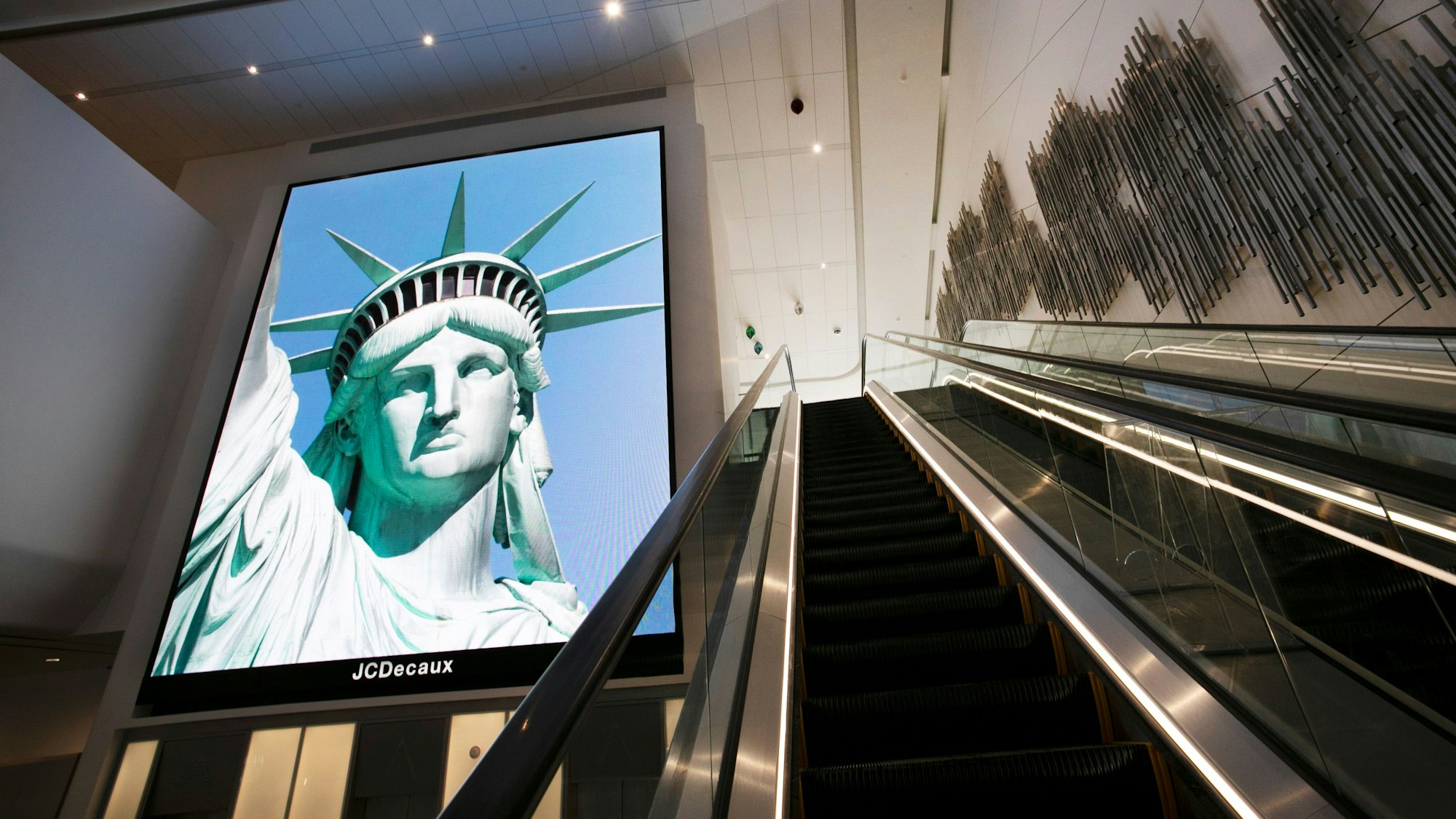 Ein elektronisches Bildschirmbild der Freiheitsstatue begrüßt ankommende Reisende auf einer Rolltreppe im Terminal B des Flughafens LaGuardia.