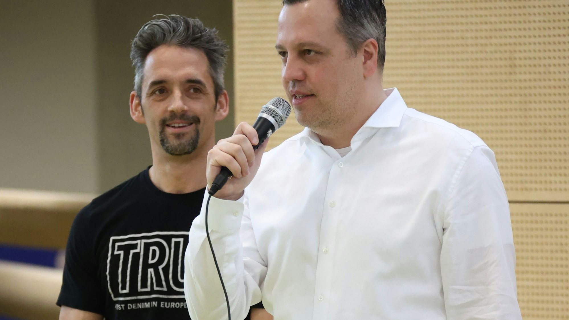 Bürgermeister Sacha Reichelt hält ein Mikrofon in der Hand. Neben ihm steht Manuél Heister.